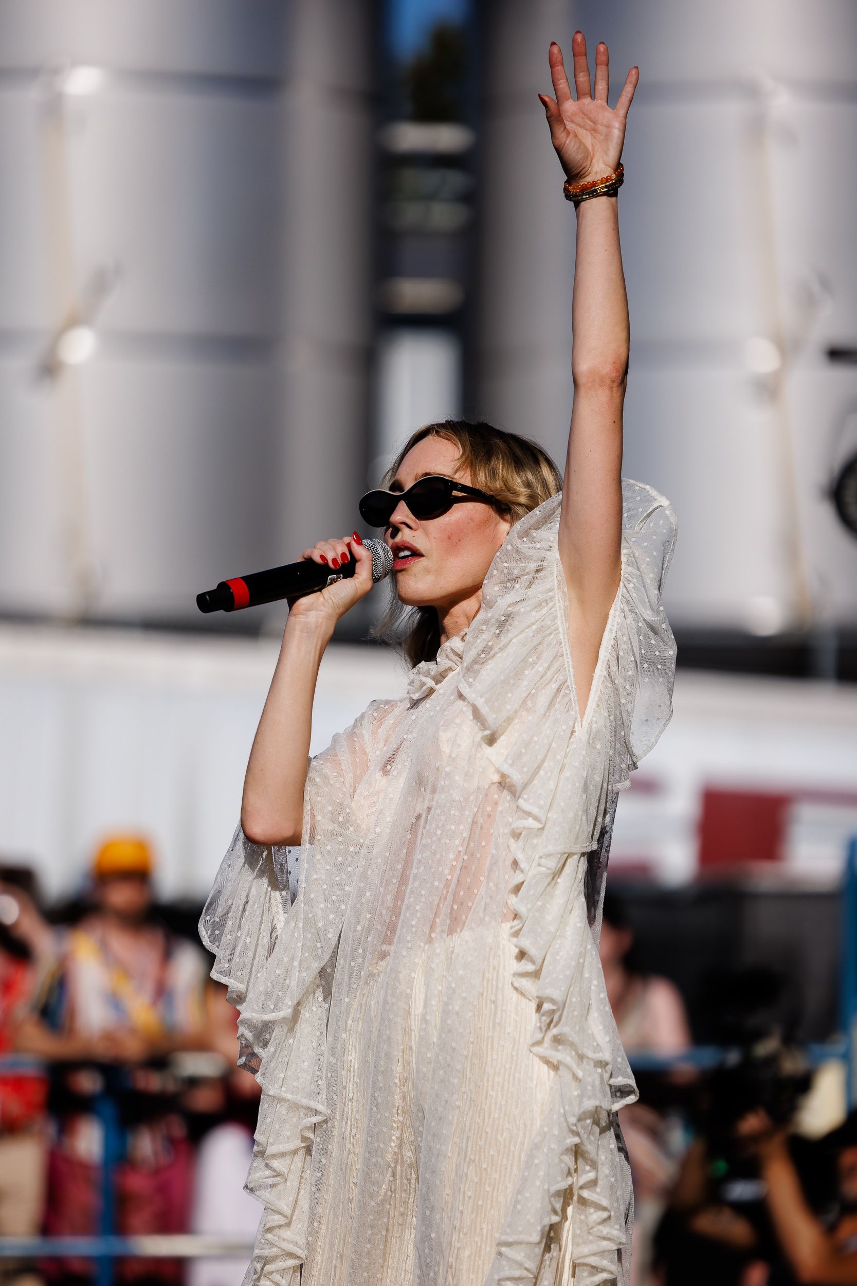 Artist in a veil and sunglasses singing with one arm raised