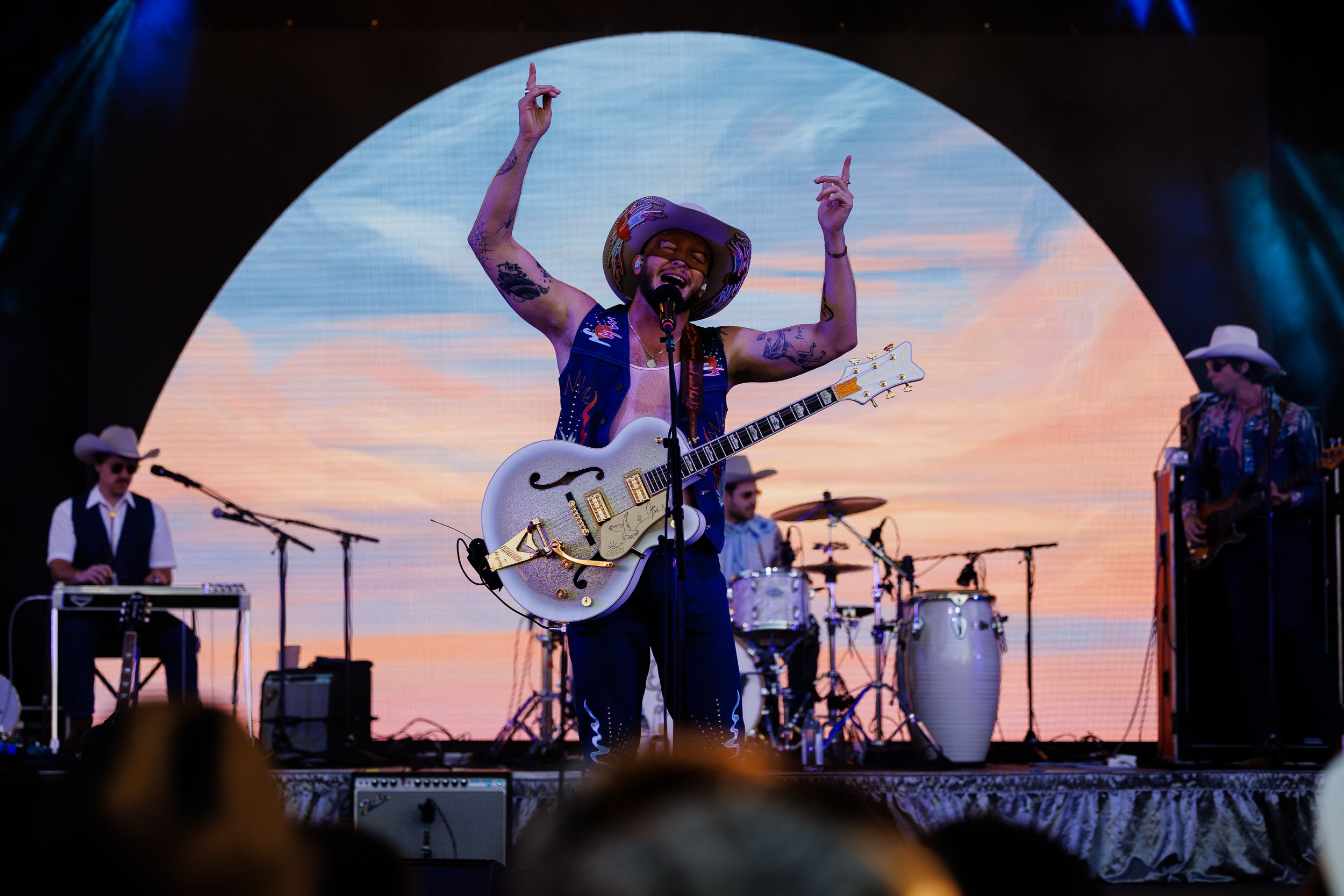 Orville Peck performing under an arched stage screen at sunset at the Phillips Backyarder festival