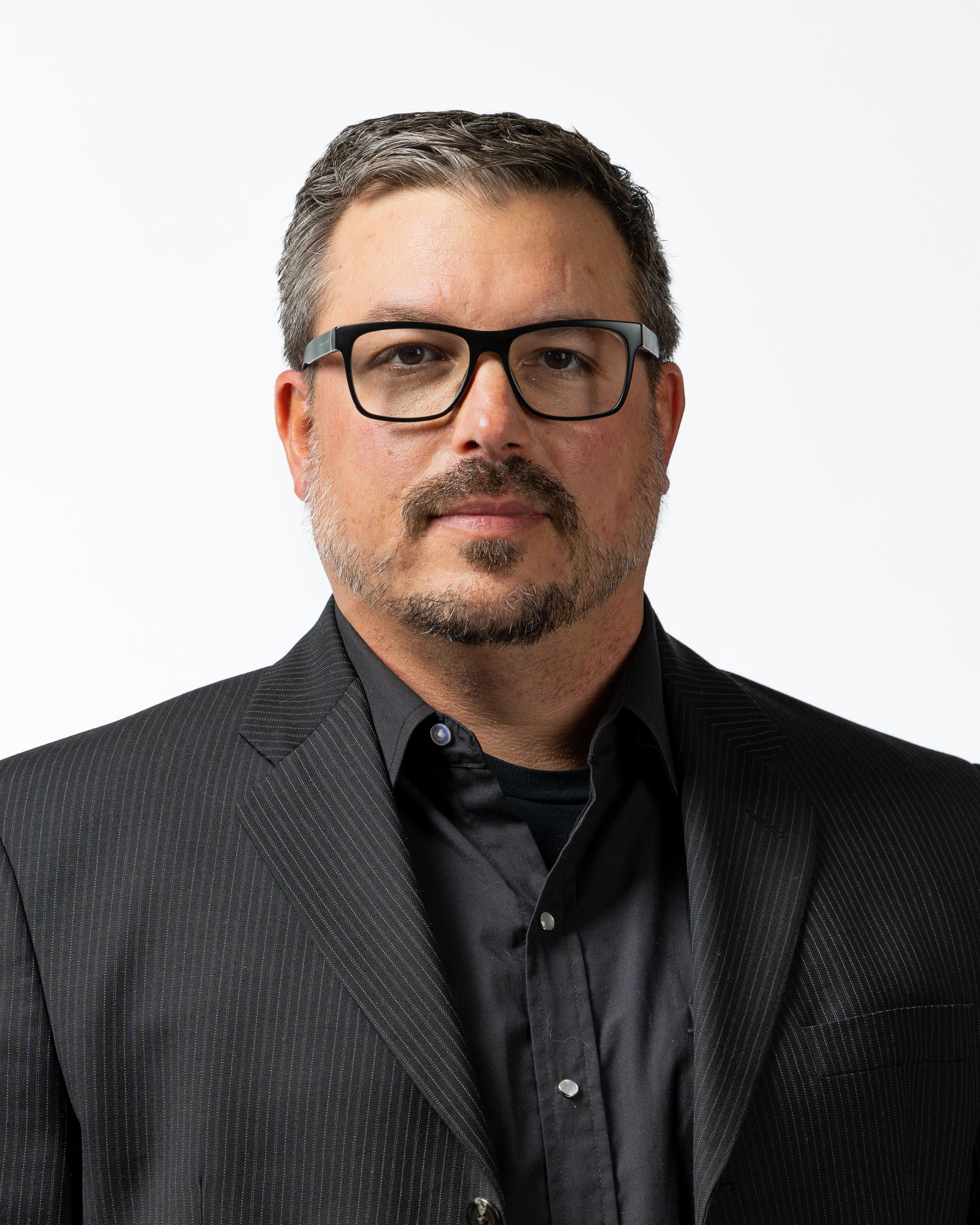 Professional headshot of a man in glasses and a dark blazer