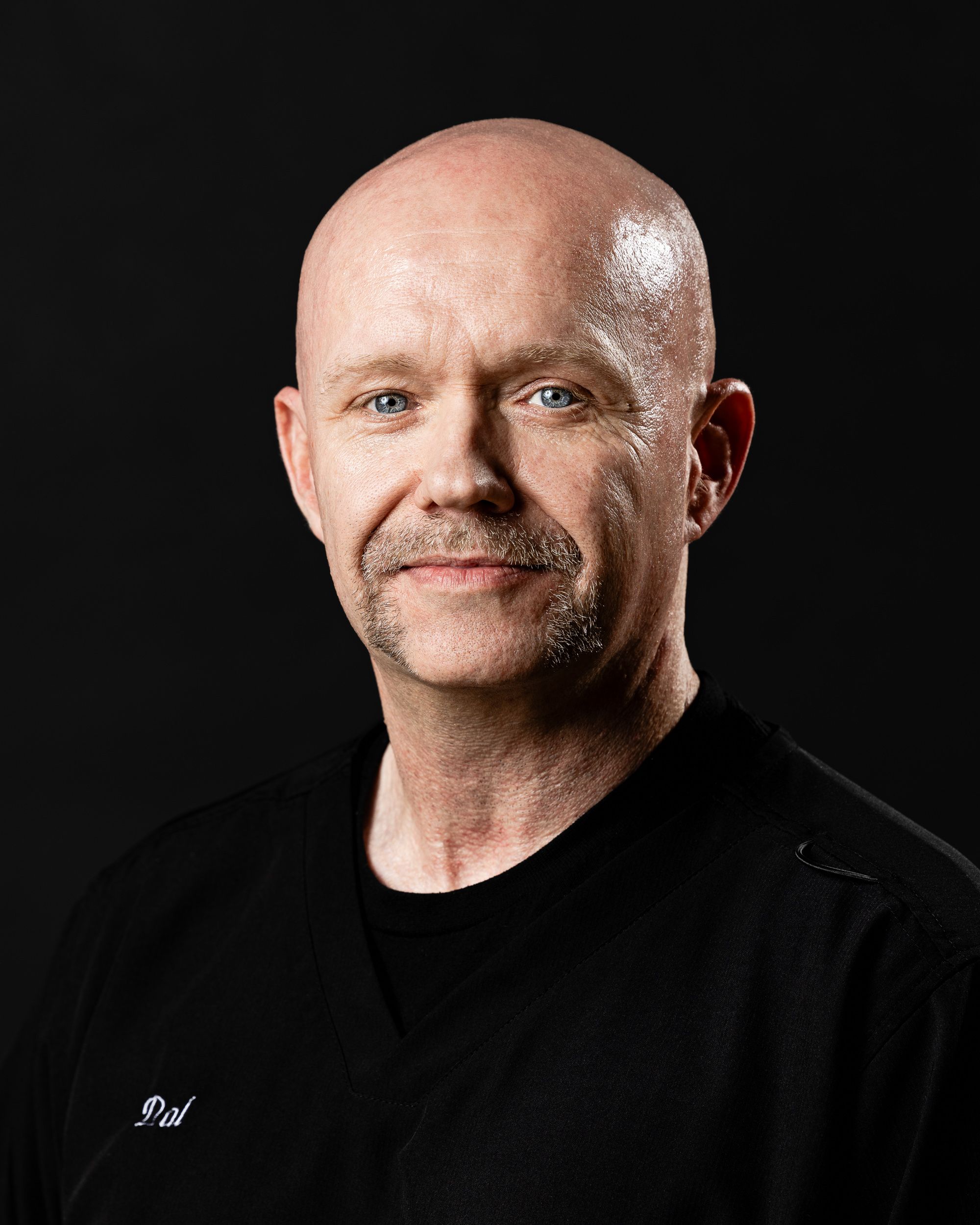 Dark-background professional headshot of a man in black