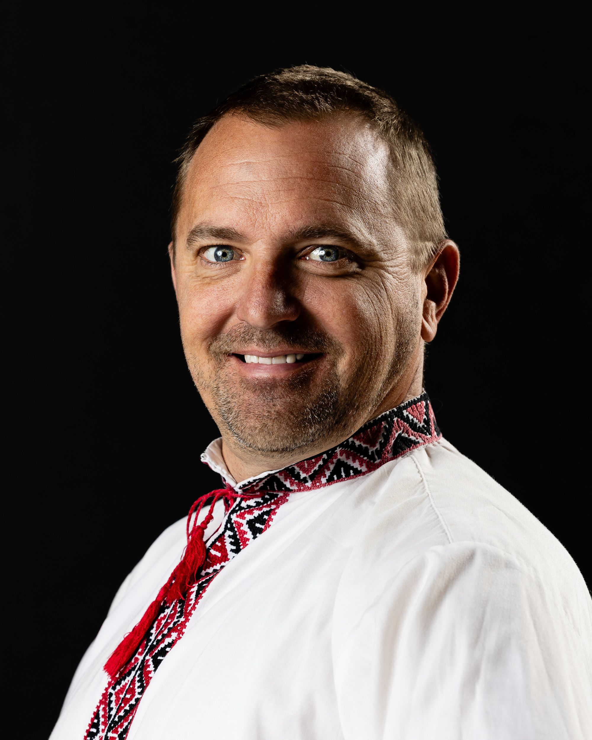 Dramatic dark-background portrait of a man in an embroidered shirt