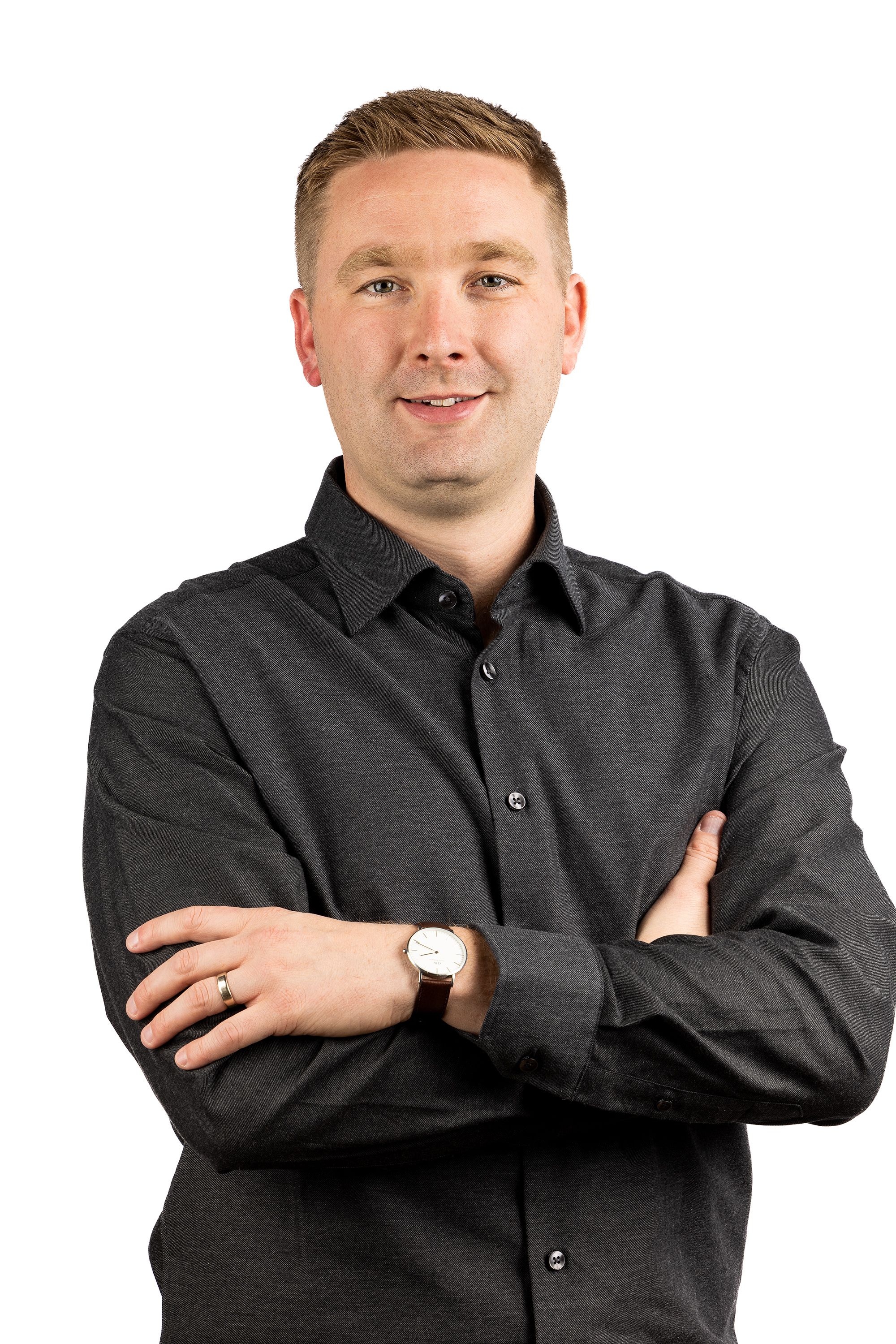 Professional headshot of a man in a dark shirt with arms crossed