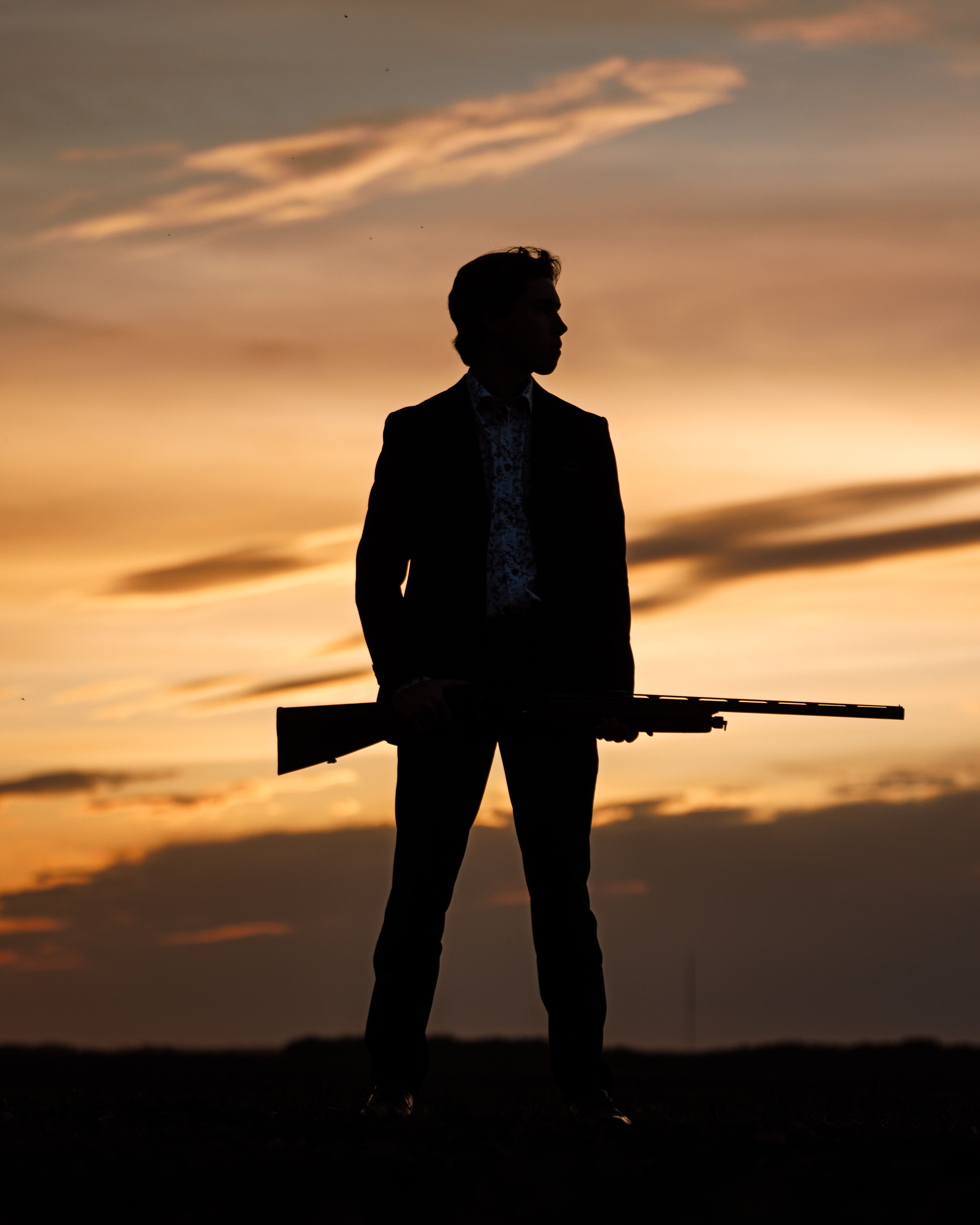 Grad silhouetted against a prairie sunset holding a shotgun