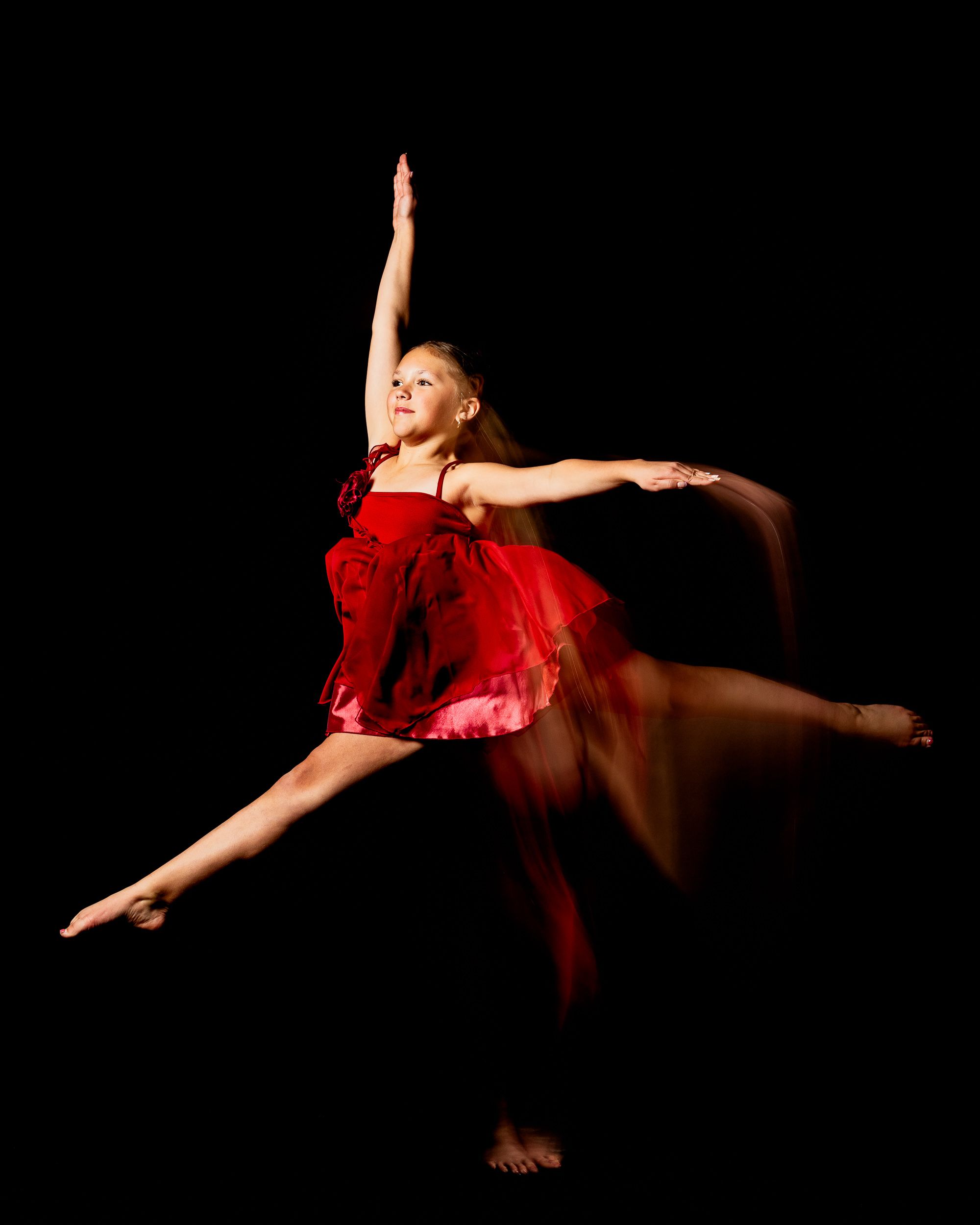Dancer in red mid-leap with motion trails on a dark stage