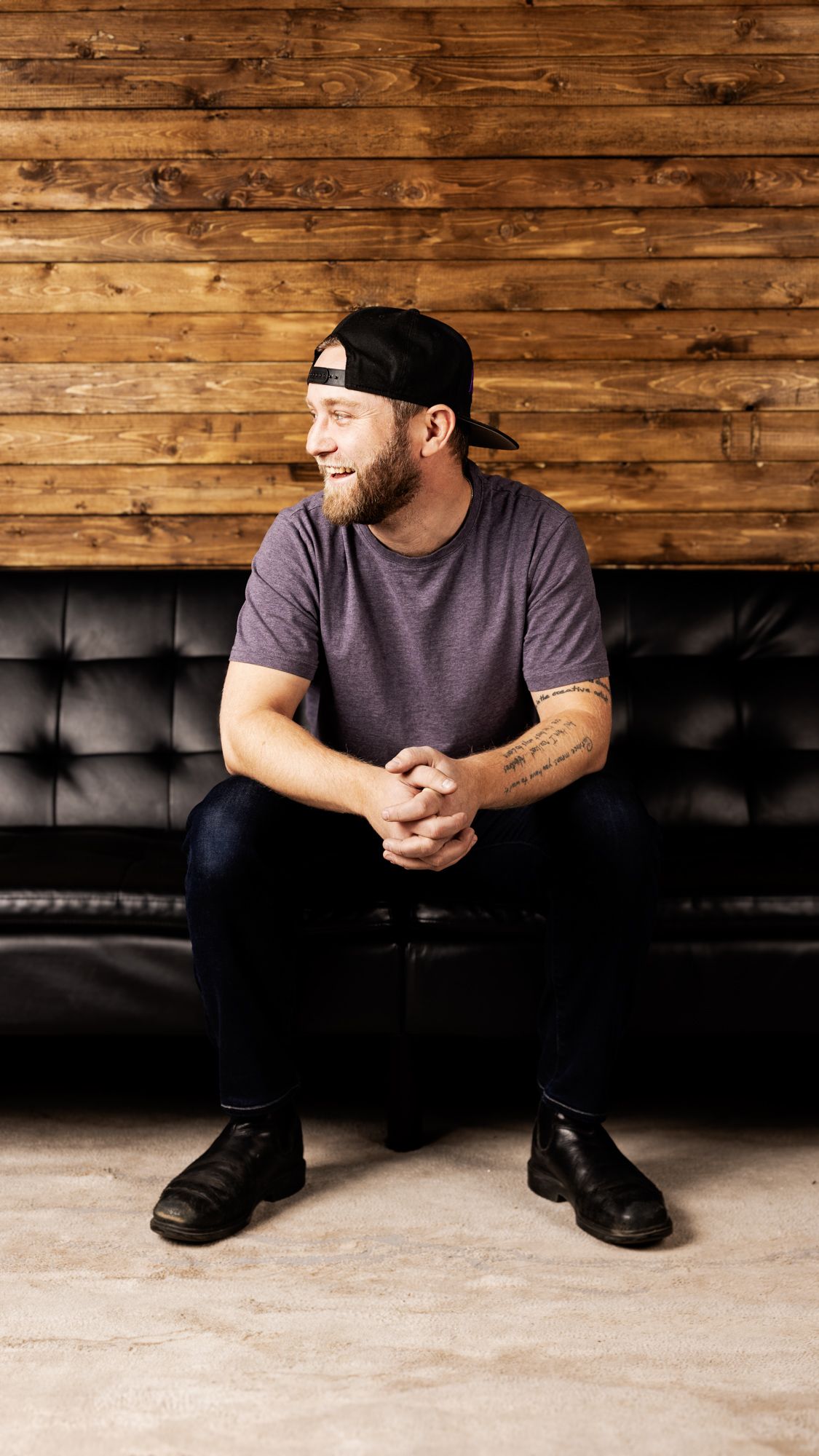 Cary Ellis seated on a leather couch against a barnwood wall, camera in hand