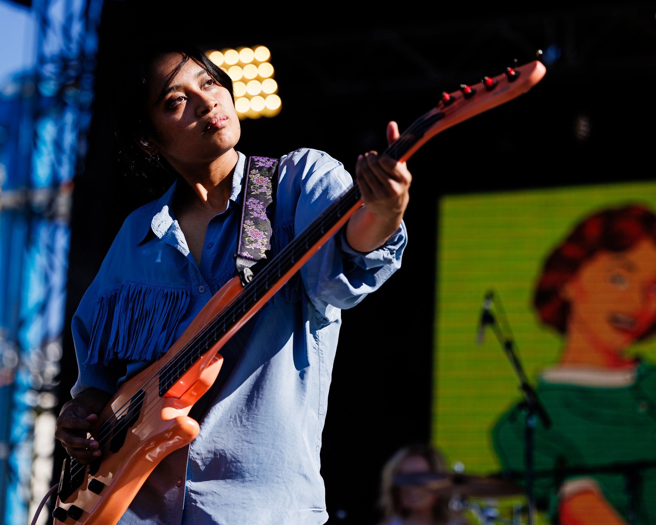 Bassist in blue fringe performing on a colourful festival stage