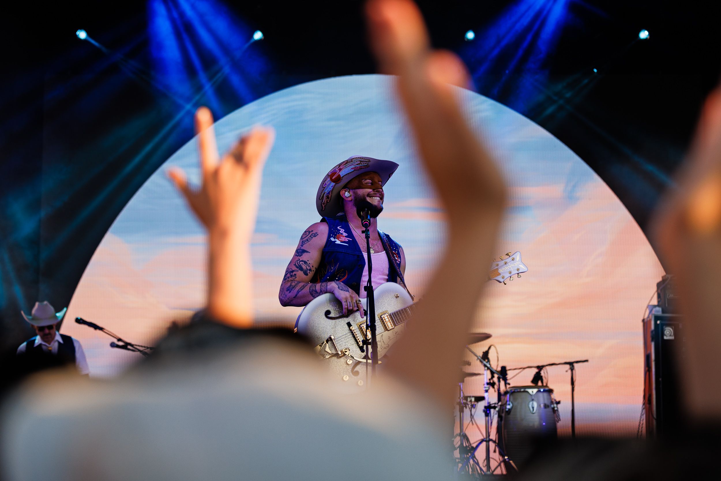 Orville Peck performing under an arched screen with fans' hands raised in the crowd
