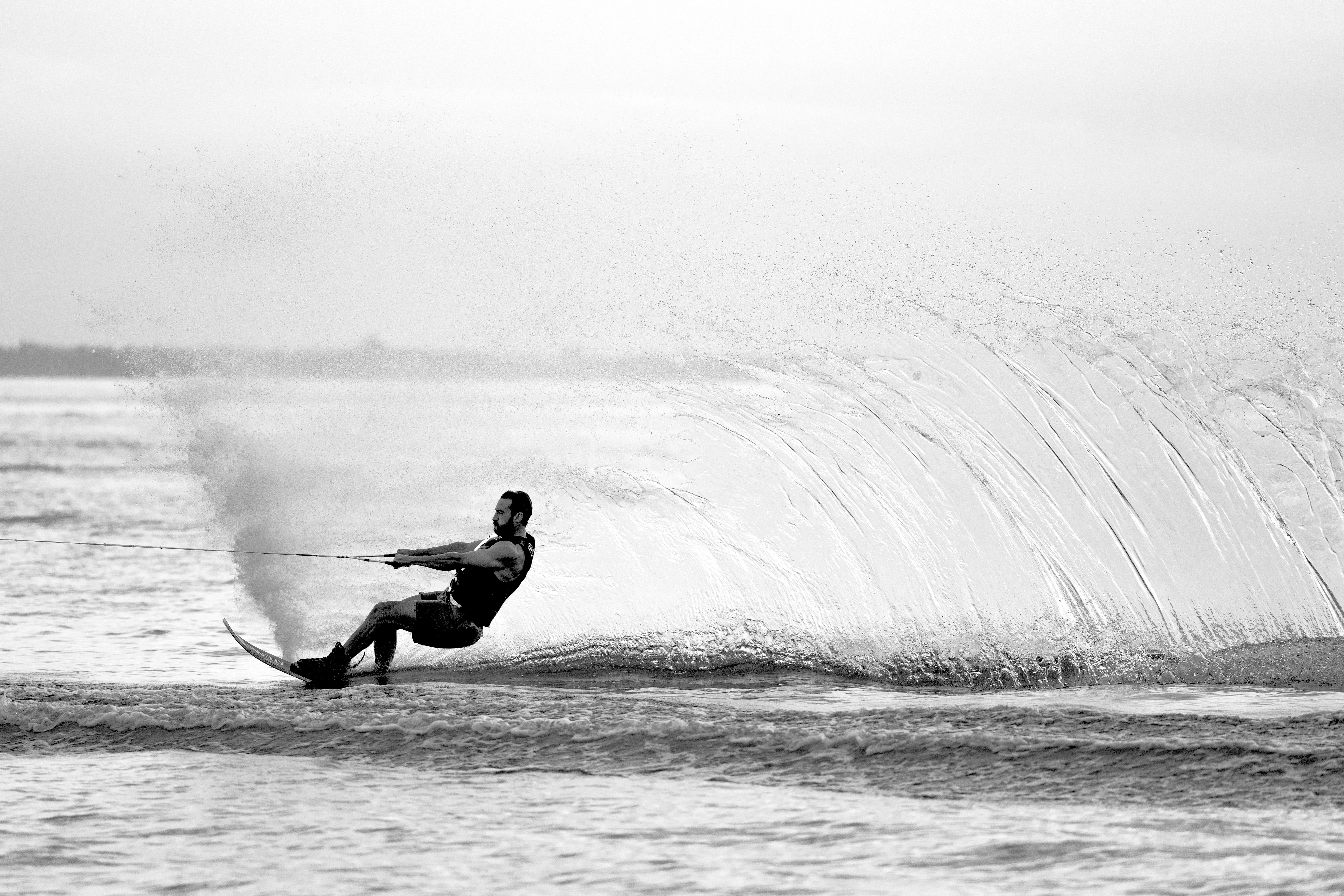 Black and white photograph of a water skier carving through a wall of spray