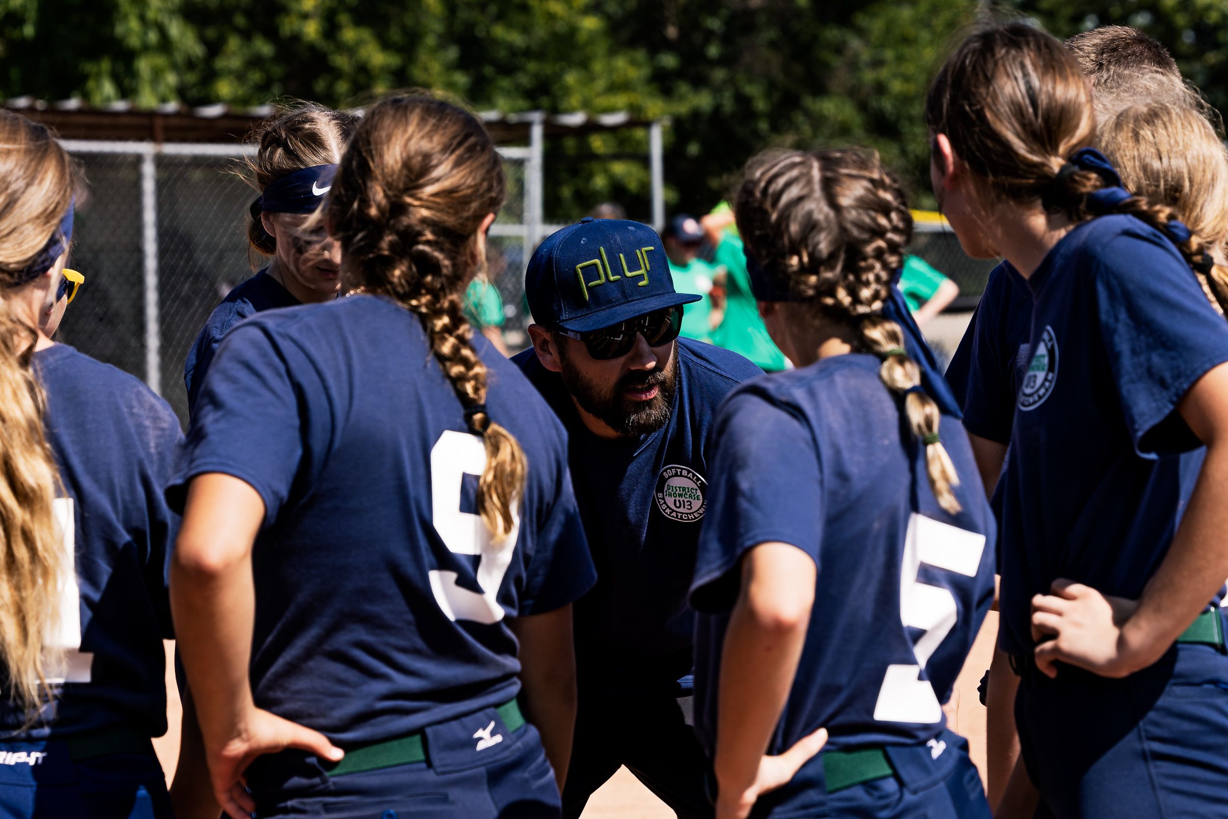U13 softball team gathered in a huddle with their coach on the diamond