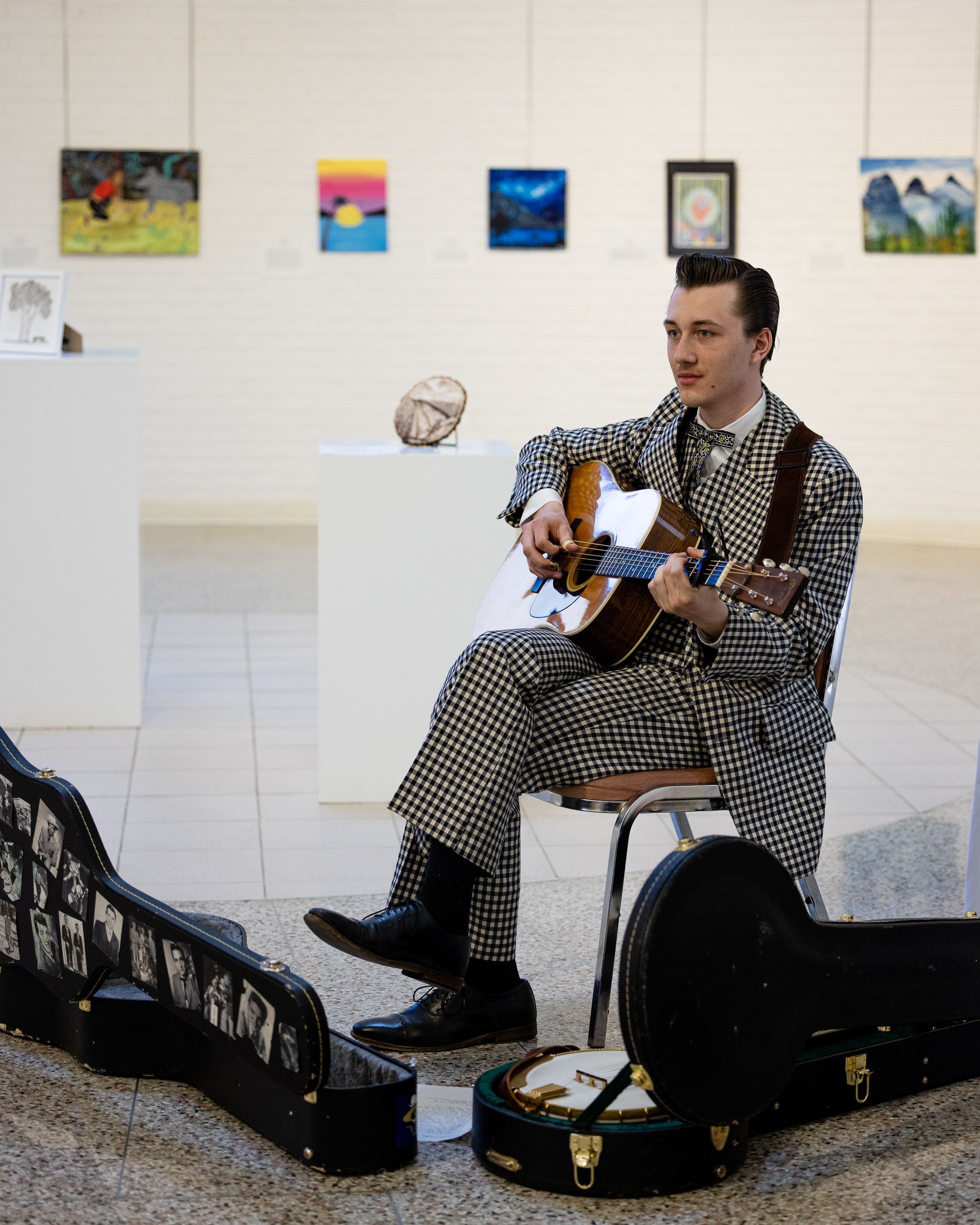 Musician playing guitar beside artwork at the Hazee Youth Art Competition